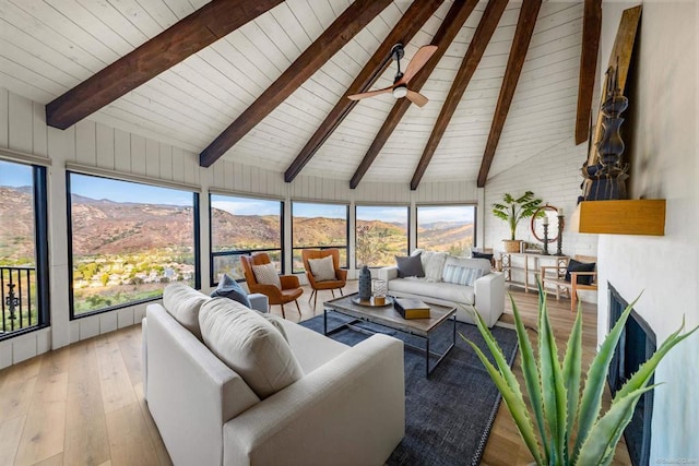 sunroom with a mountain view, a wealth of natural light, vaulted ceiling with beams, and ceiling fan