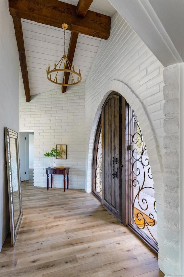 foyer entrance featuring vaulted ceiling with beams, light hardwood / wood-style flooring, brick wall, and a notable chandelier