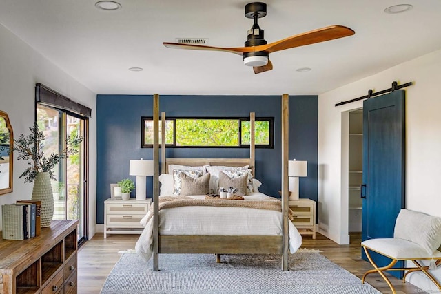 bedroom featuring a barn door, ceiling fan, wood-type flooring, and multiple windows