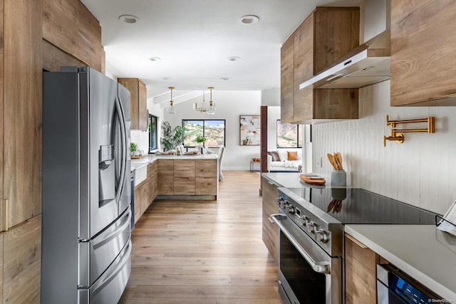 kitchen with light wood-type flooring, appliances with stainless steel finishes, pendant lighting, and wall chimney exhaust hood