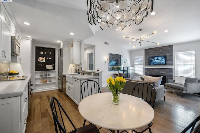 dining area with sink, dark hardwood / wood-style floors, a tiled fireplace, and vaulted ceiling