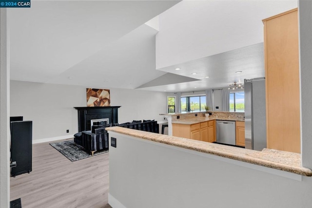 kitchen featuring kitchen peninsula, appliances with stainless steel finishes, light brown cabinets, a chandelier, and light hardwood / wood-style flooring