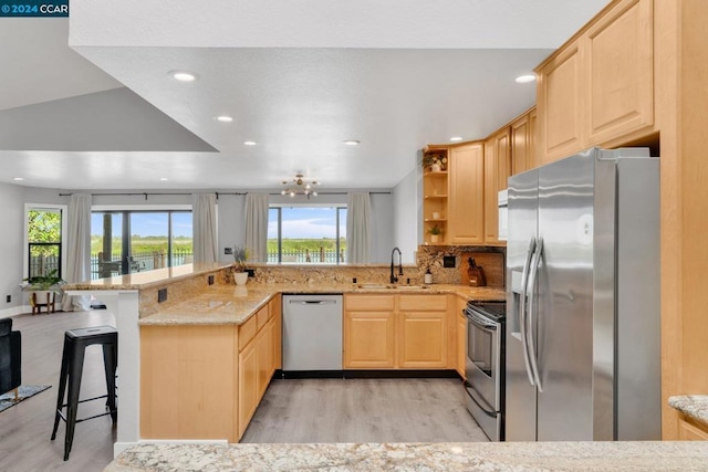 kitchen with light brown cabinets, stainless steel appliances, a kitchen breakfast bar, sink, and kitchen peninsula