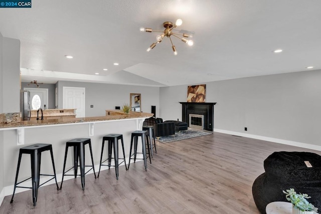 kitchen featuring light hardwood / wood-style floors, stainless steel fridge, kitchen peninsula, a notable chandelier, and a breakfast bar area