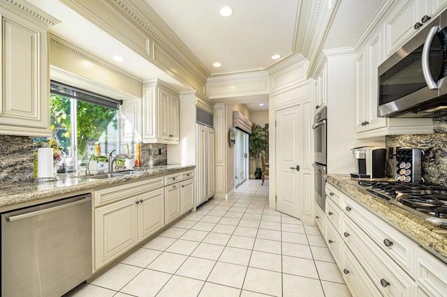 kitchen with cream cabinetry, appliances with stainless steel finishes, backsplash, light stone countertops, and sink