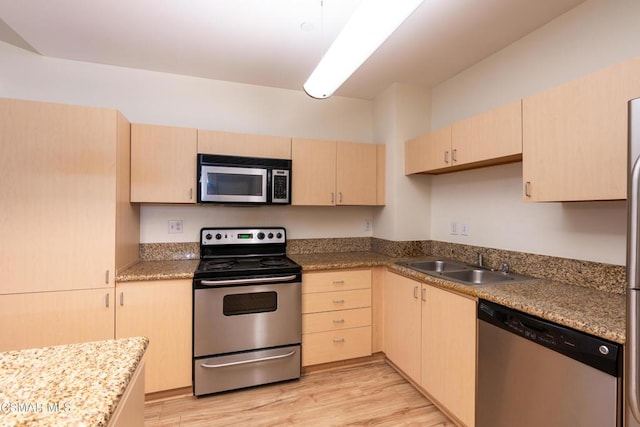 kitchen with stone counters, sink, light wood-type flooring, stainless steel appliances, and light brown cabinetry