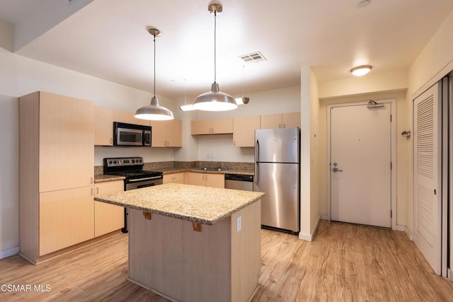 kitchen with a kitchen island, pendant lighting, light wood-type flooring, light stone countertops, and appliances with stainless steel finishes