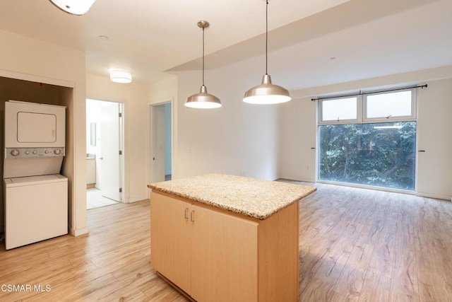 kitchen with decorative light fixtures, light hardwood / wood-style flooring, stacked washing maching and dryer, light brown cabinetry, and light stone counters