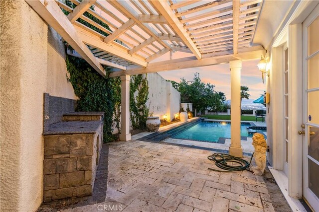 pool at dusk featuring a pergola and a patio