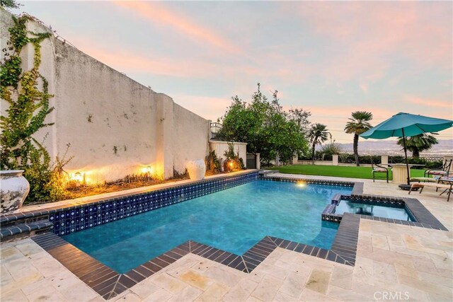 pool at dusk featuring an in ground hot tub and a patio area