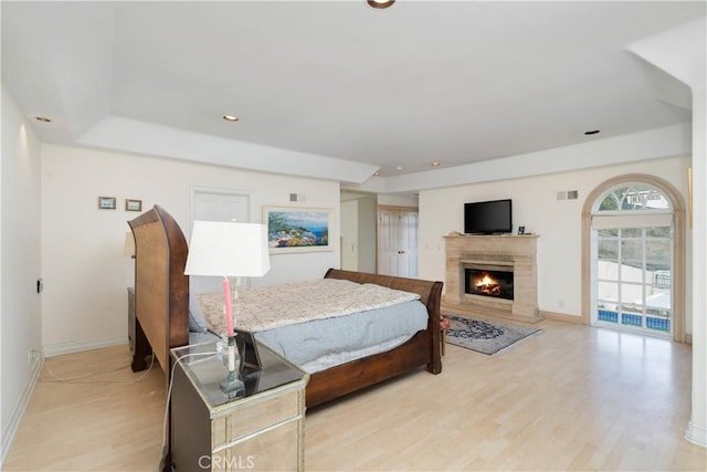 bedroom with a high end fireplace, light hardwood / wood-style flooring, and a tray ceiling