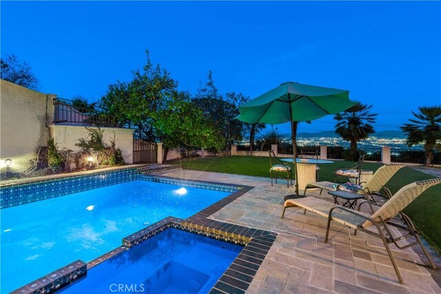 pool at dusk featuring a patio area, an in ground hot tub, and a yard