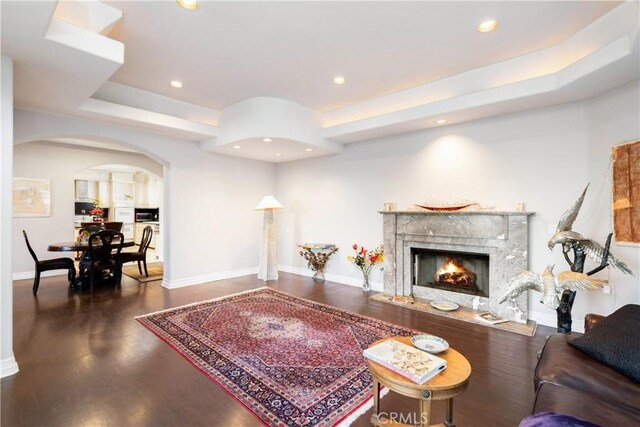 living room with a tray ceiling, dark hardwood / wood-style floors, and a fireplace