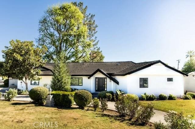 ranch-style home featuring a front lawn, a tile roof, and stucco siding