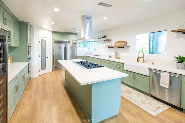 kitchen with visible vents, island range hood, stainless steel appliances, green cabinets, and a sink