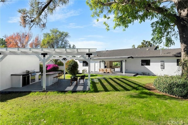 rear view of property featuring a lawn, outdoor dry bar, exterior kitchen, a pergola, and stucco siding