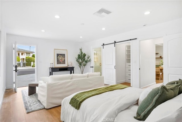 bedroom with a spacious closet, light wood-style flooring, recessed lighting, and a barn door