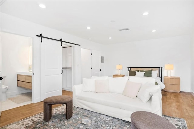 bedroom with recessed lighting, visible vents, a barn door, connected bathroom, and wood finished floors