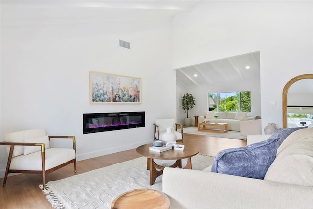 living area featuring high vaulted ceiling, a glass covered fireplace, beamed ceiling, and wood finished floors