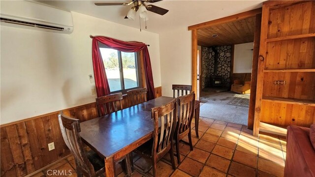 dining area with an AC wall unit, a wood stove, ceiling fan, and wooden walls