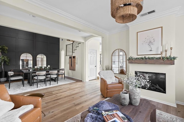 living area featuring arched walkways, wood finished floors, visible vents, stairs, and crown molding