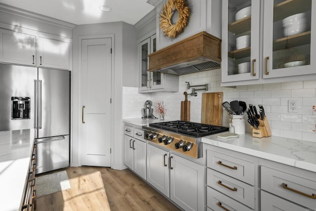 kitchen with light wood-type flooring, appliances with stainless steel finishes, decorative backsplash, and light stone counters