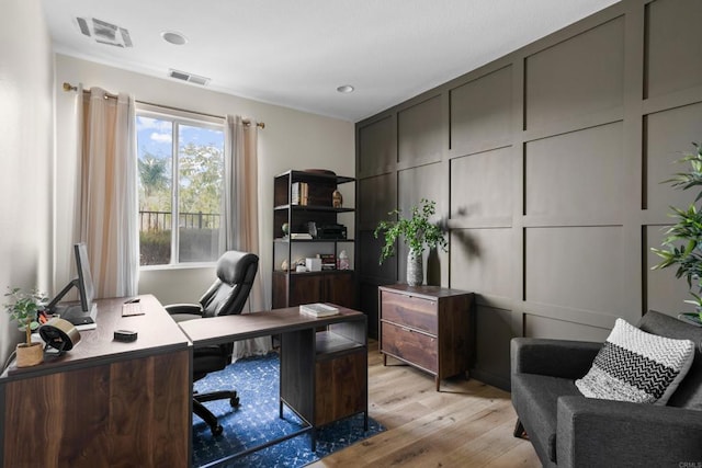 home office featuring light wood-type flooring, visible vents, and a decorative wall