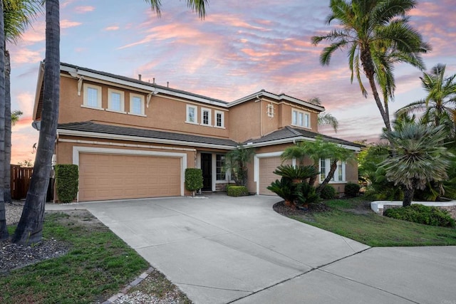 traditional home with driveway, an attached garage, a tiled roof, and stucco siding