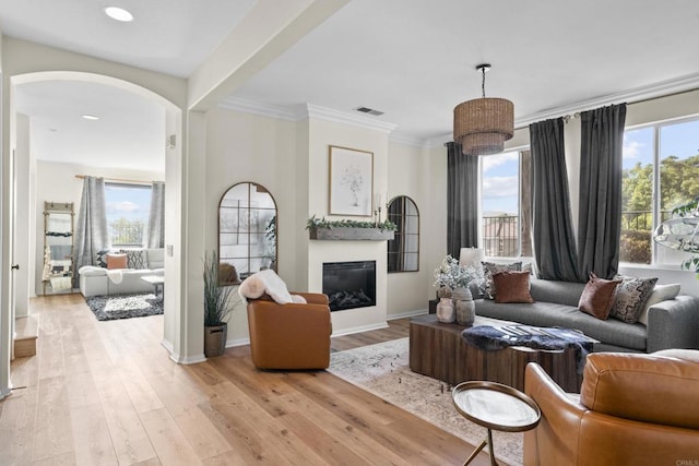 living room with ornamental molding, a glass covered fireplace, light wood-style flooring, and baseboards