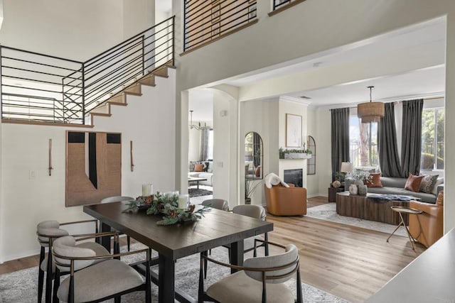 dining space featuring a glass covered fireplace, baseboards, a high ceiling, and light wood finished floors