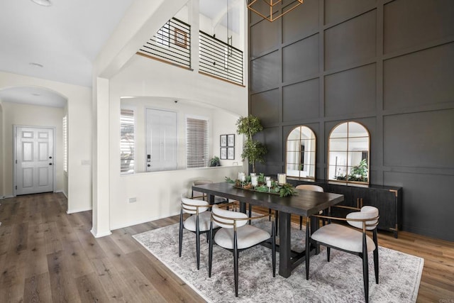 dining area featuring arched walkways, a decorative wall, and wood finished floors