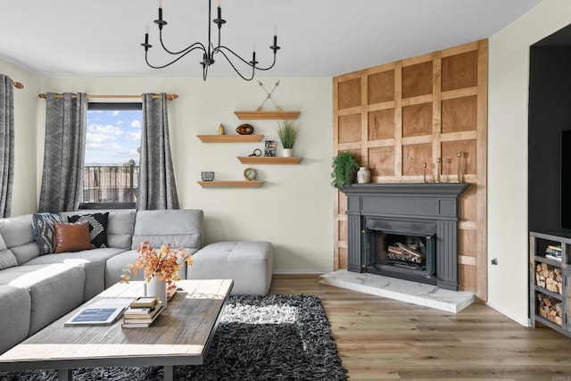 living room with a fireplace with raised hearth, baseboards, wood finished floors, and a chandelier