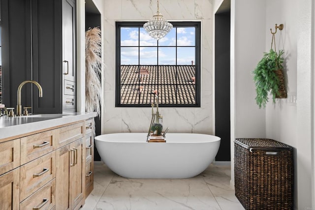 full bathroom with marble finish floor, vanity, an inviting chandelier, and a soaking tub