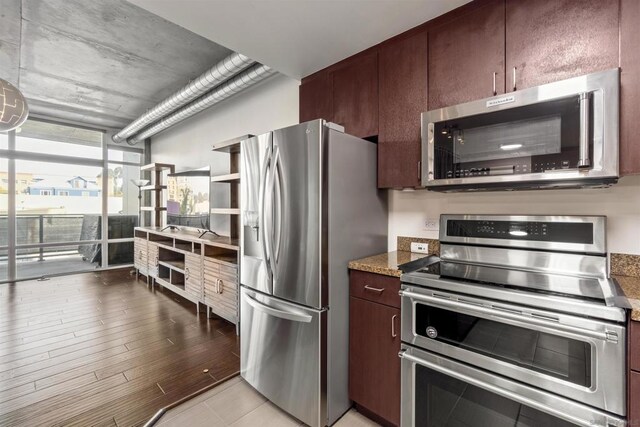 kitchen featuring dark stone countertops, dark brown cabinetry, light hardwood / wood-style flooring, stainless steel appliances, and a wall of windows