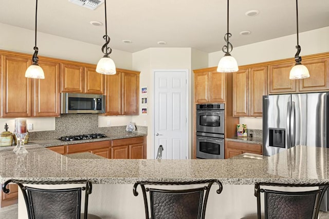 kitchen with appliances with stainless steel finishes, decorative light fixtures, backsplash, light stone counters, and a breakfast bar area