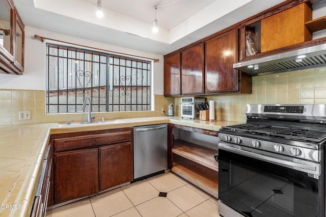 kitchen with appliances with stainless steel finishes, tile counters, sink, light tile patterned floors, and a tray ceiling