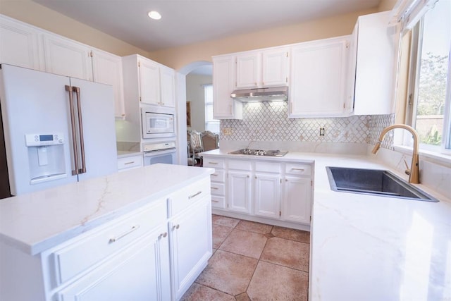 kitchen with white cabinetry, decorative backsplash, white appliances, light stone countertops, and sink