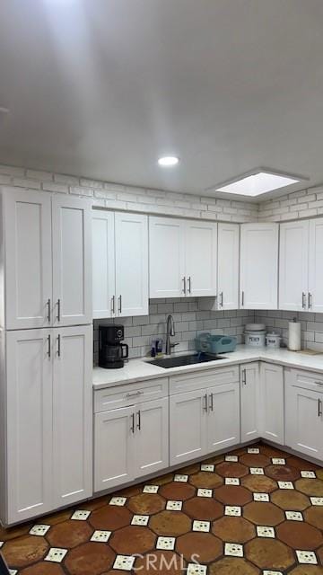 kitchen featuring sink, white cabinetry, backsplash, and a skylight