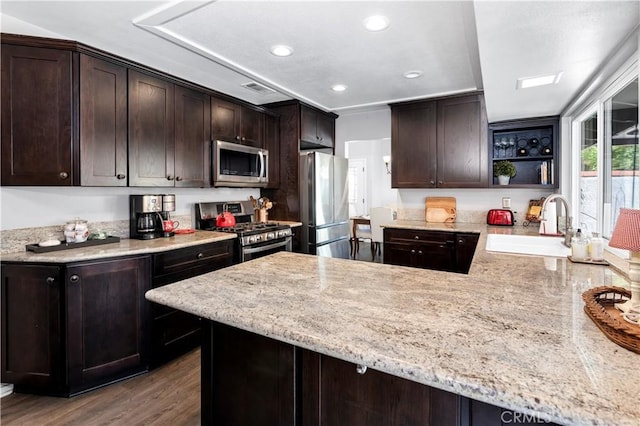 kitchen with kitchen peninsula, dark brown cabinets, light stone countertops, stainless steel appliances, and dark hardwood / wood-style flooring