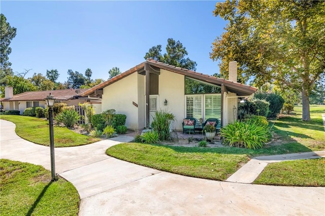 view of front of house with stucco siding, a chimney, and a front yard