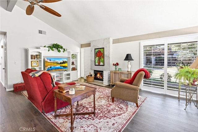 living room featuring ceiling fan, dark wood-type flooring, a large fireplace, and high vaulted ceiling