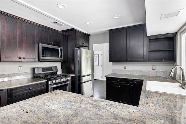 kitchen with a sink, visible vents, appliances with stainless steel finishes, light stone countertops, and open shelves