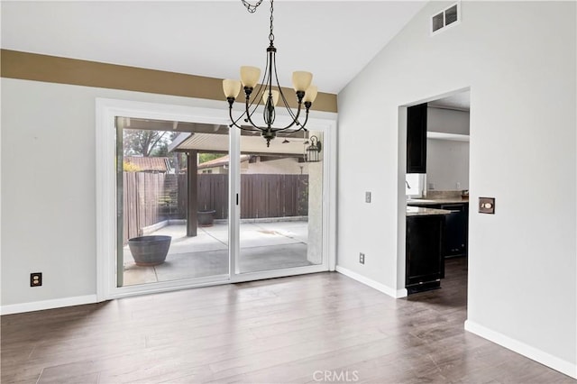 unfurnished dining area featuring baseboards, visible vents, vaulted ceiling, and wood finished floors