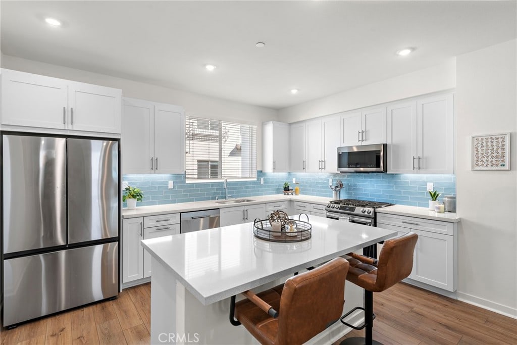 kitchen with appliances with stainless steel finishes, a kitchen island, white cabinetry, light wood-type flooring, and a breakfast bar