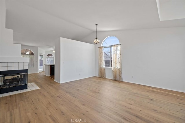 unfurnished living room with lofted ceiling, a tile fireplace, ceiling fan with notable chandelier, and light hardwood / wood-style floors