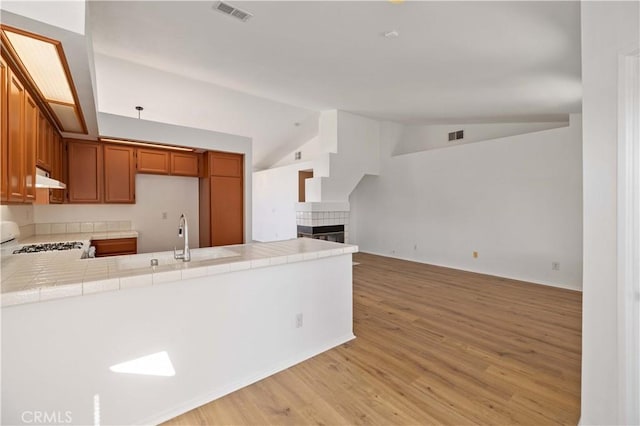 kitchen featuring tile countertops, a fireplace, kitchen peninsula, and sink