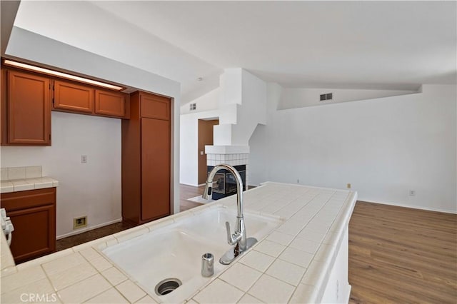 kitchen with tile counters, a fireplace, light hardwood / wood-style floors, and lofted ceiling