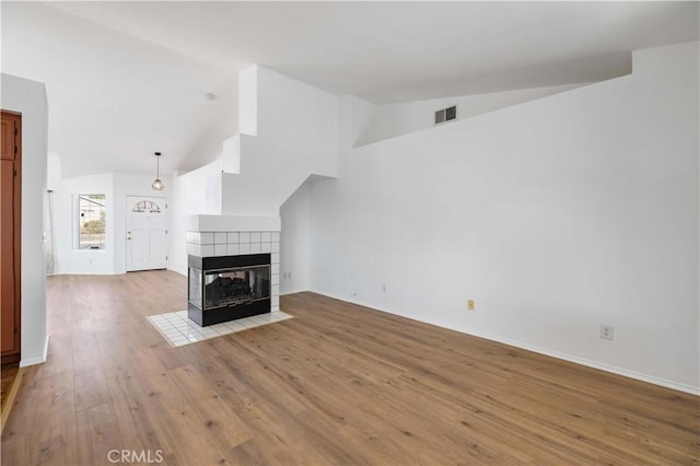 unfurnished living room with light hardwood / wood-style flooring, lofted ceiling, and a tiled fireplace