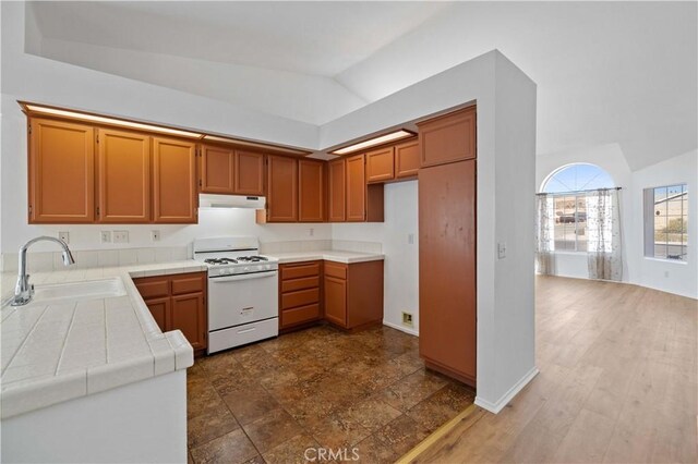 kitchen with vaulted ceiling, tile countertops, white range, and sink