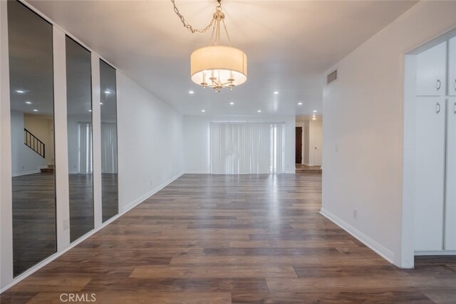 spare room with a notable chandelier and dark hardwood / wood-style flooring